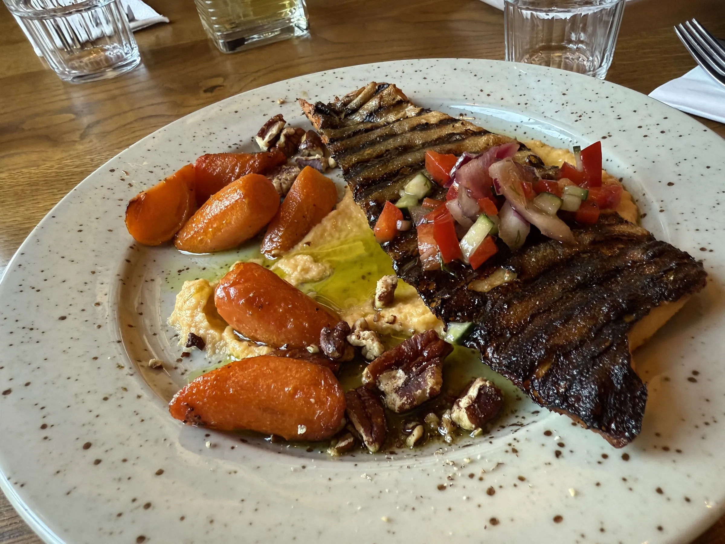 Plate of charred Arctic char with crisp grill marks, served with roasted carrots, fresh tomato salsa, pecans, and yogurt