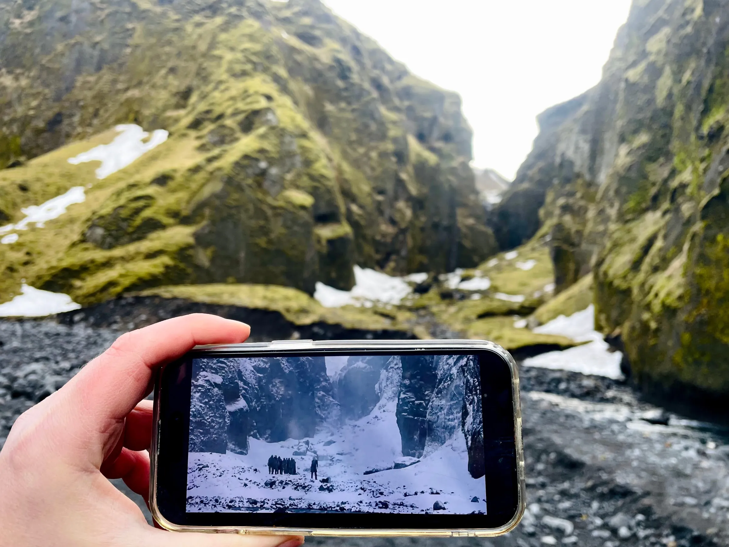 Hand holding up a phone showing a Game of Thrones White Walkers still inside the actual mossy snow-dusted canyon where the scene was shot