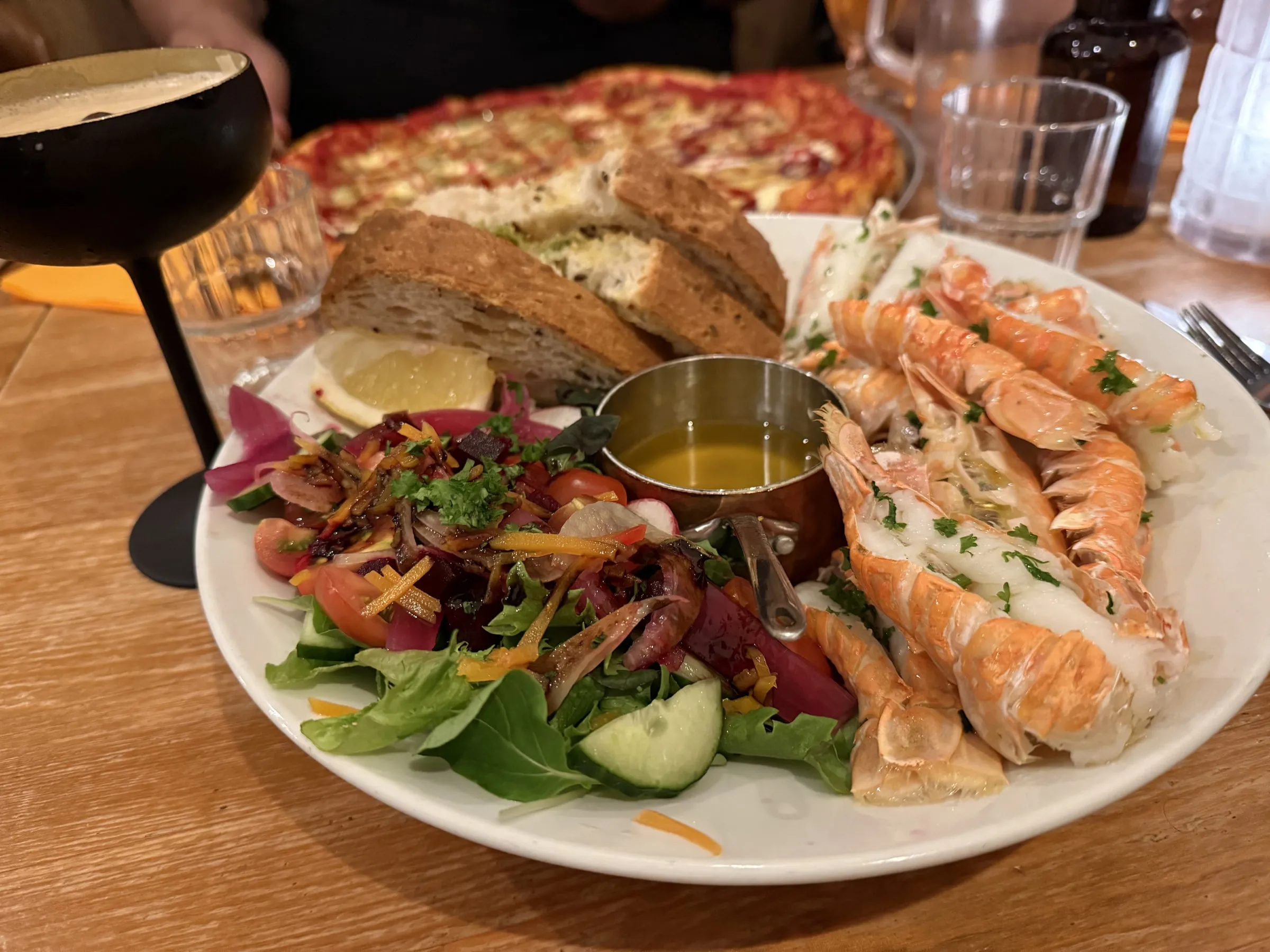 Plate of fresh Icelandic langoustines with brown bread, dressed salad, lemon, melted butter, and a glass of dark stout